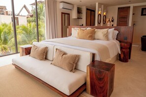 Ein geräumiges Schlafzimmer mit einem großen Bett, einer Schlafcouch und Blick auf Palmen.