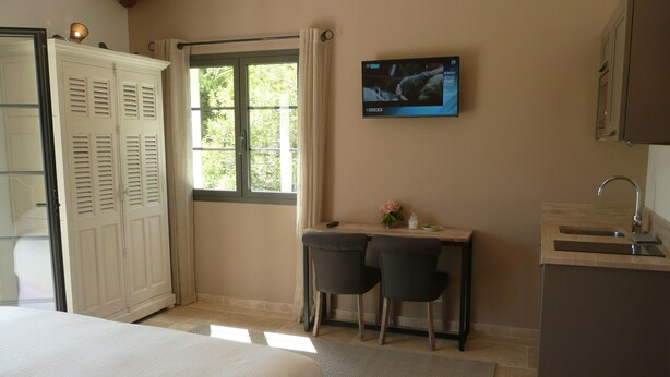 A bedroom with a bed, a desk with two chairs, a TV, and a bathroom with a sink. - Etoile De Saint Paul (Saint-Paul-de-Vence)