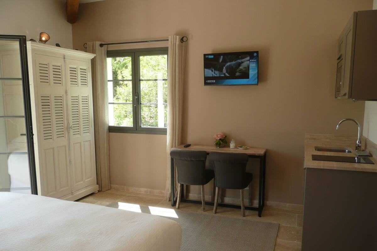 A bedroom with a bed, a desk with two chairs, a TV, and a bathroom with a sink.