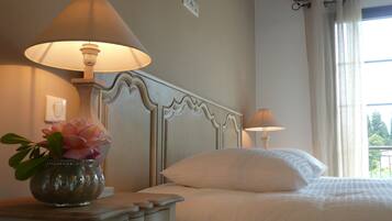 A bedroom with a bed, two bedside lamps, a nightstand with a vase of flowers, and a window with curtains.