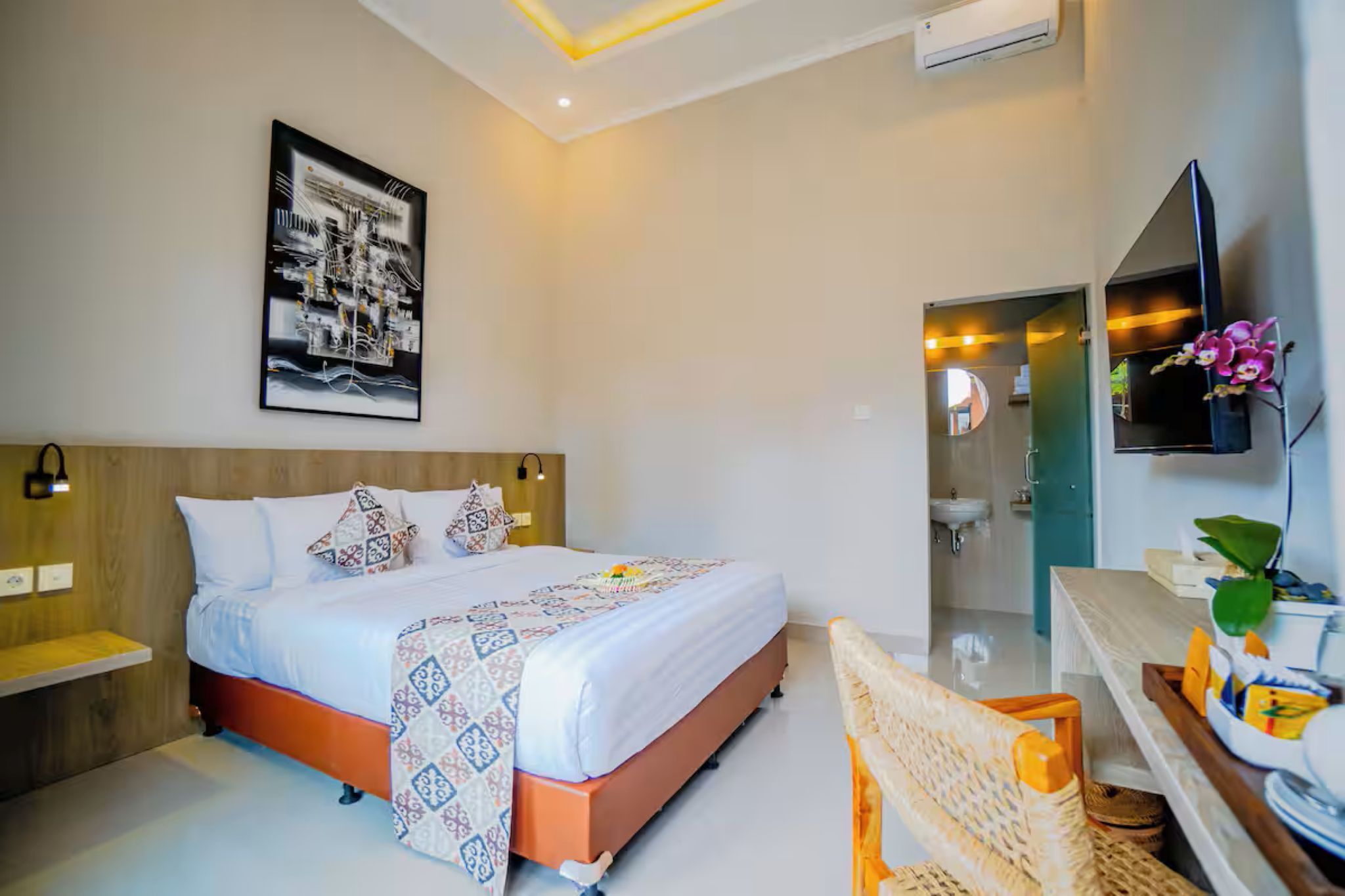 A modern hotel room with a large bed, bedside tables, a mounted TV, and a bathroom visible through an open door.