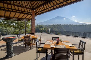 An outdoor dining area with tables and chairs, a decorative stone planter, and a view of a mountain. - Tapa Agung View Hotel & Restaurant (Rendang)