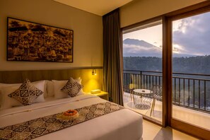 A hotel room with a large bed, a painting on the wall, a balcony with a table and chairs, and a mountain view. - Tapa Agung View Hotel & Restaurant (Rendang)