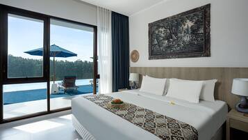 A hotel room with a large bed, a view of the sea, a painting on the wall, and a balcony with a chair and umbrella.