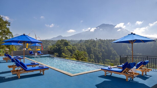 A poolside area with lounge chairs and umbrellas, overlooking a mountainous landscape.