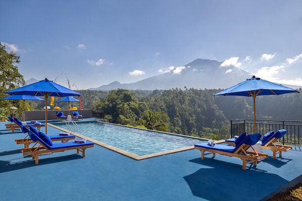 A poolside area with lounge chairs and umbrellas, overlooking a mountainous landscape.