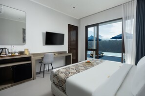 A hotel room with a bed, a desk, a chair, a TV, and a view of a pool and mountains. - Tapa Agung View Hotel & Restaurant (Rendang)