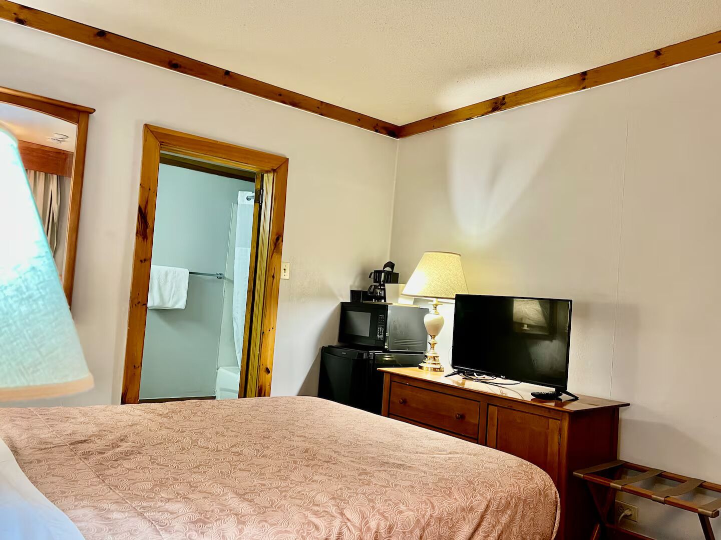 A hotel room with a bed, a television on a wooden dresser, a lamp, and a mirror.