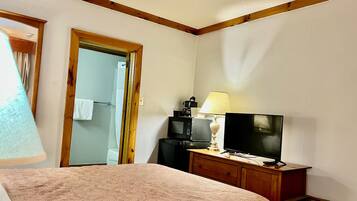A hotel room with a bed, a television on a wooden dresser, a lamp, and a mirror.