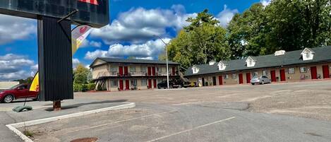 A motel with a sign reading "The Rocky Mountain." It features a two-story building with multiple rooms, a parking lot, and a clear blue sky with clouds.