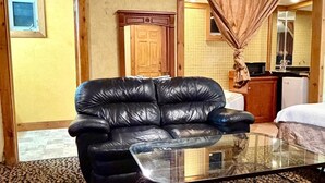 A room with a black leather sofa, a glass coffee table, and a patterned carpet.