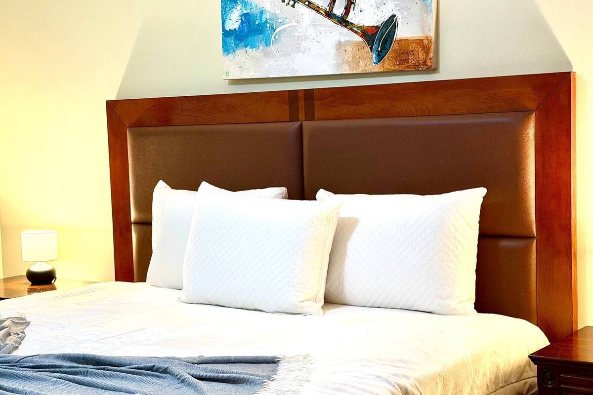 A hotel room with a large bed, white bedding, a wooden headboard, and a painting above the bed.