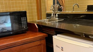 A kitchen with a black microwave, a white refrigerator, a wooden cabinet, and a stainless steel sink.