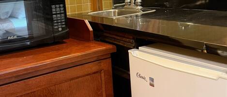 A kitchen with a black microwave, a white refrigerator, a wooden cabinet, and a stainless steel sink.