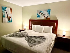 A hotel room with a large bed, two bedside tables with lamps, and two paintings on the walls. - Rocky Mountain Lodge & Suites (Renfrew)