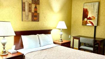 Habitación de hotel con cama, dos lámparas de noche, un escritorio con silla y dos cuadros en las paredes.