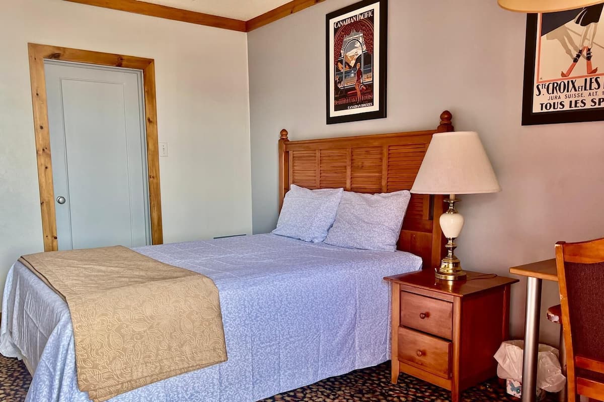 A bedroom with a bed, a nightstand, a lamp, a chair, and a door.