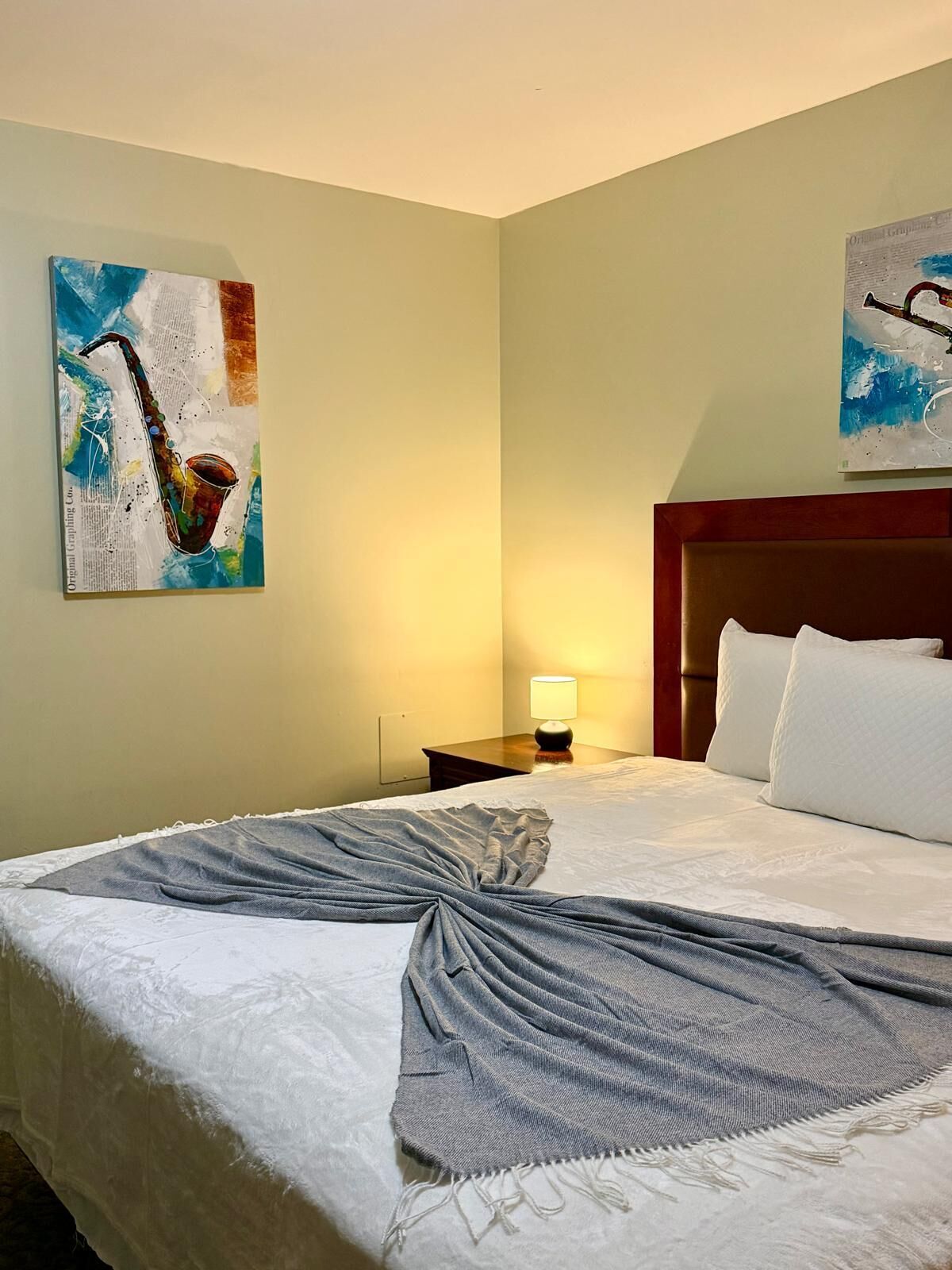 A hotel room with a bed, a nightstand, a lamp, and two wall art pieces.