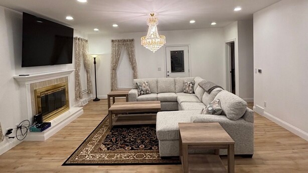 Un salon moderne avec un canapé d’angle, un téléviseur à écran plat, une cheminée et un lustre.