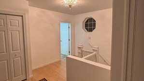 Un couloir doté d’un plancher en bois, d’un tapis à motifs, d’une porte blanche et d’un escalier avec une rampe blanche.