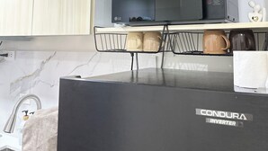 A kitchen with wooden cabinets, a black microwave, and a black refrigerator with a 'CONDURA INVERTER' label. - Cozy, Spacious 1-bedroom Condo in Novaliches, Perfect for Staycations & Creators (Quezon City)