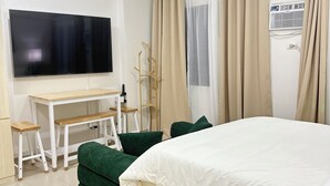 A hotel room with a bed, a desk, a chair, a TV, and a window with curtains. - Cozy, Spacious 1-bedroom Condo in Novaliches, Perfect for Staycations & Creators (Quezon City)