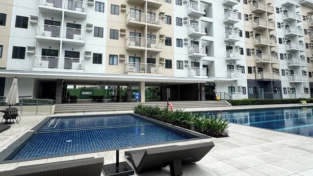 A modern apartment building with multiple balconies, a swimming pool, and a covered outdoor area. - Cozy, Spacious 1-bedroom Condo in Novaliches, Perfect for Staycations & Creators (Quezon City)