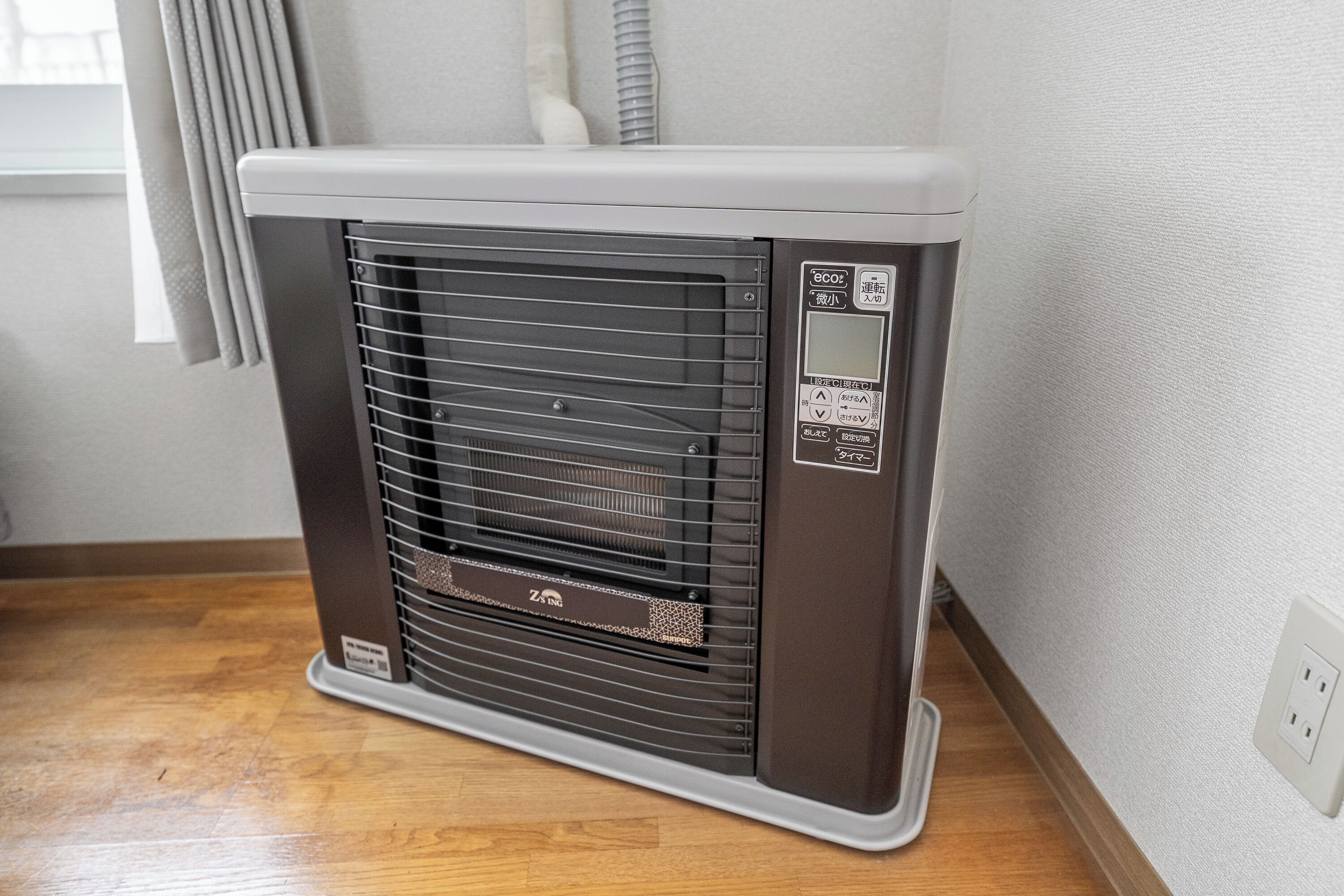 Een draagbare verwarming met een bedieningspaneel, geplaatst op een houten vloer tegen een muur.