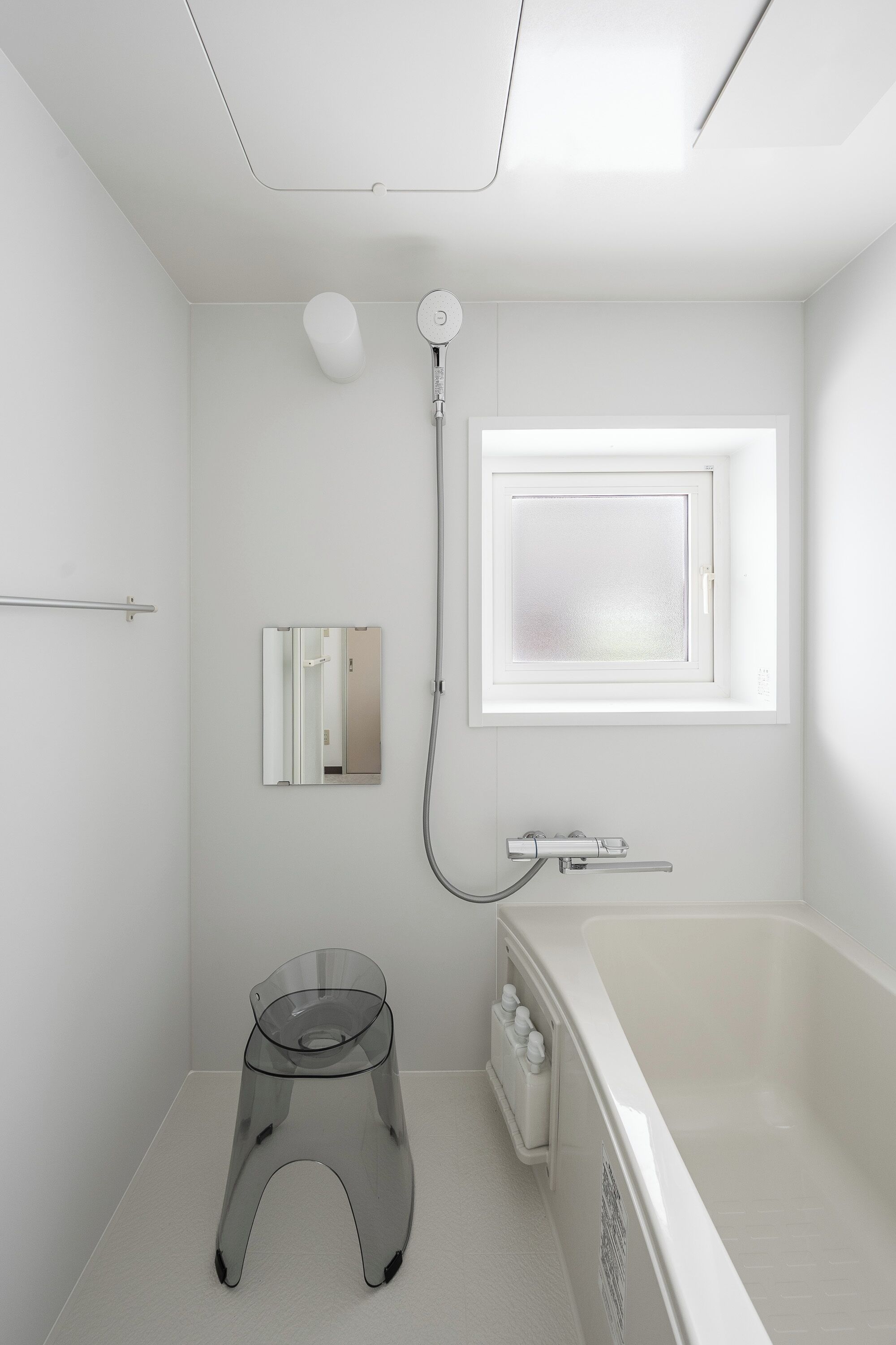 Un baño moderno con una bañera, un taburete pequeño, una ventana y un espejo.