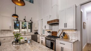 Una cucina moderna con mobili bianchi, un'isola grande in marmo e luci a sospensione.