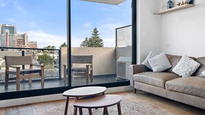 A modern living room with a large window, a sofa, a small table, and a balcony with chairs. - One-Bed Apartment Close to Cafés and Coast (Port Melbourne)