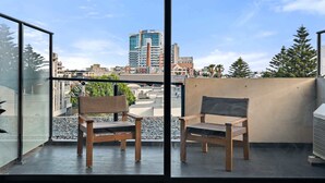 A balcony with two wooden chairs, a view of a cityscape, and a building in the background. - One-Bed Apartment Close to Cafés and Coast (Port Melbourne)