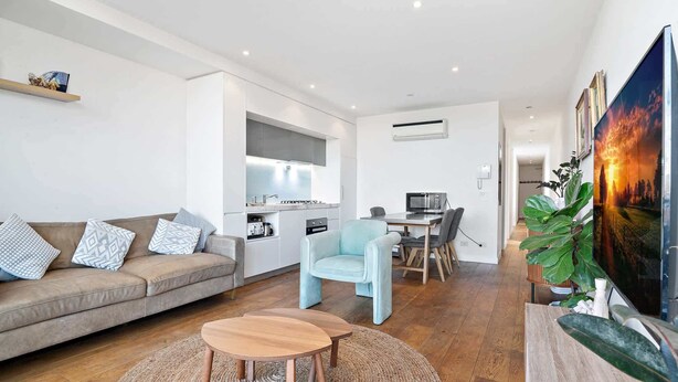 A modern living room with a sofa, a light blue armchair, a wooden coffee table, and a TV. - One-Bed Apartment Close to Cafés and Coast (Port Melbourne)