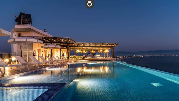 A infinity pool with a view of the sea, a covered outdoor seating area, and a building with a modern design. - Panarea 3D | Beachfront 4BR + Ocean Views & Pools (Bucerías)