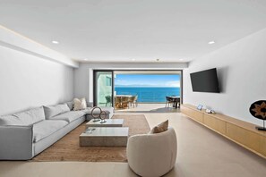A modern living room with a large sofa, a coffee table, and a TV mounted on the wall. - 4BR w/ Oceanfront Views, Gym & Pools | Panarea 5D (Bucerías)