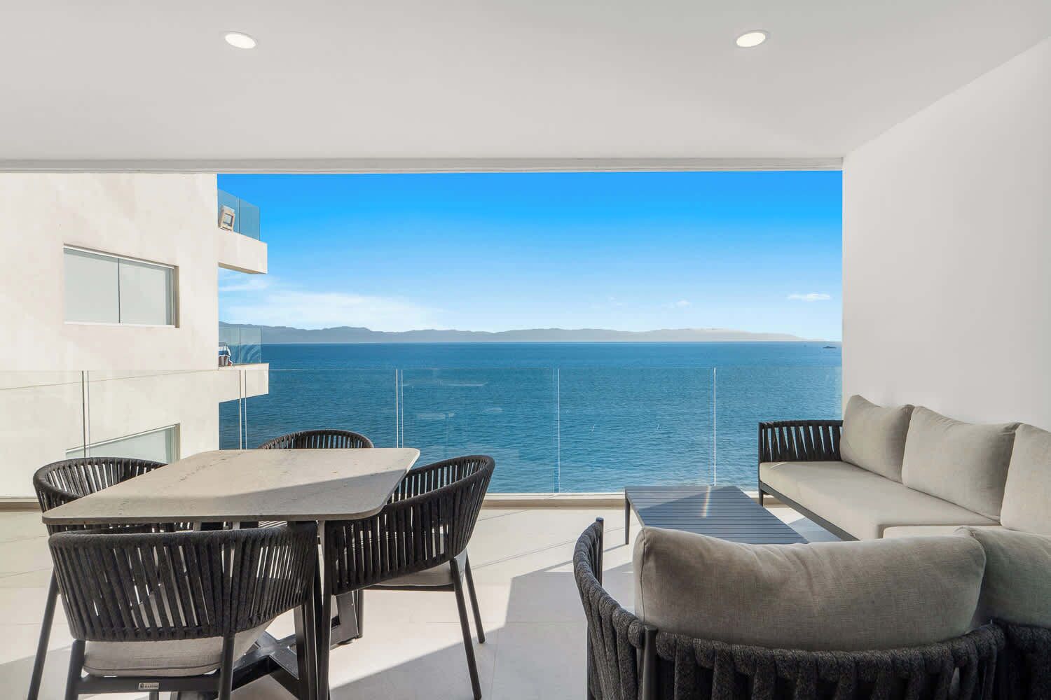 Un balcon avec une table et des chaises, un canapé et une vue sur la mer.