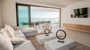 Een moderne woonkamer met een grote schuifpui die uitkomt op een balkon met uitzicht op zee.