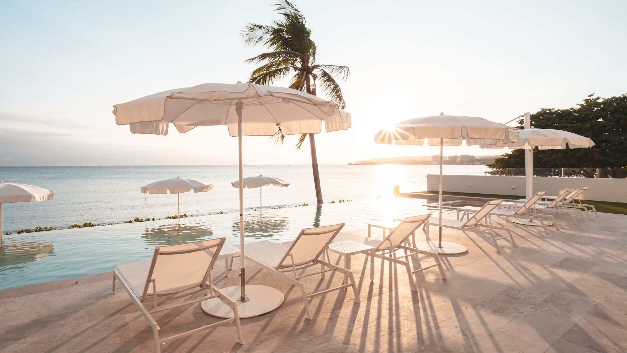 A poolside area with lounge chairs and umbrellas, overlooking a body of water.