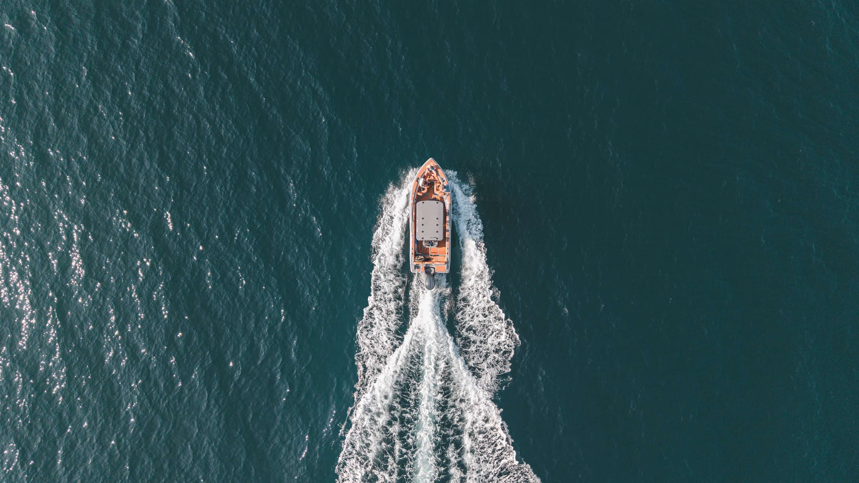 An aerial view of a boat moving through the water, creating a wake behind it.
