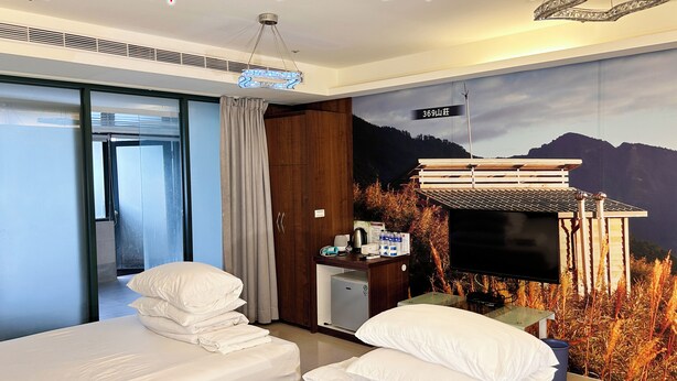 Ein Hotelzimmer mit zwei Betten, einem Schreibtisch mit Fernseher, einer kleinen Minibar und einem Wandbild mit Berglandschaft.