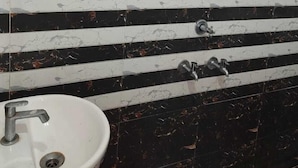 A bathroom with a white sink, black and white marble tiles, and black marble stripes. - Shubh Hotel (Phulpur)