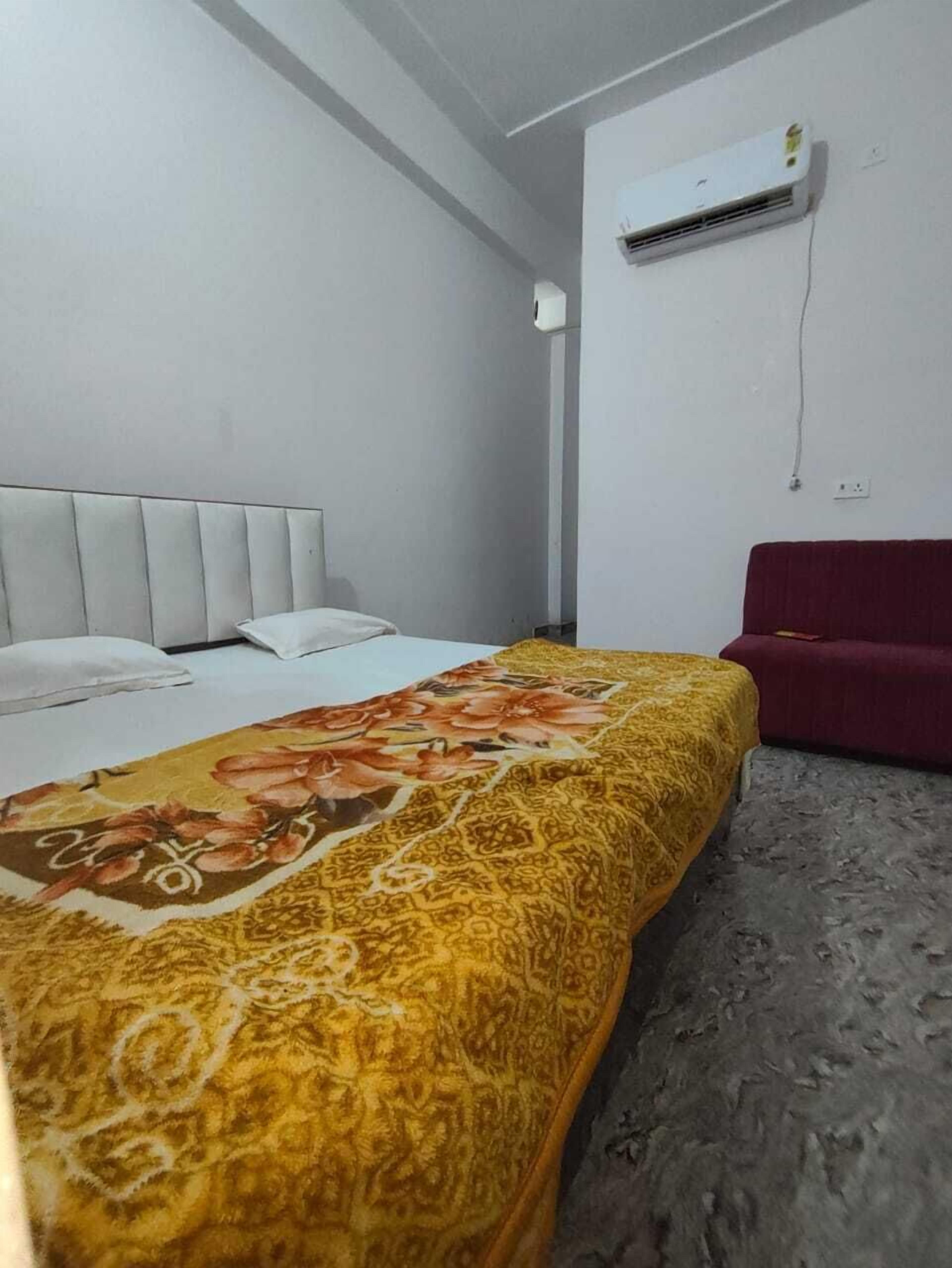 Una habitación de hotel con una cama, un sofá rojo y un equipo de aire acondicionado en la pared.