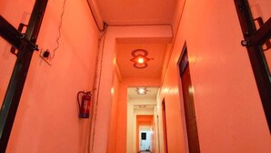 A hallway with a red-orange hue, featuring a fire alarm on the left and a light fixture on the ceiling. - Shubh Hotel (Phulpur)