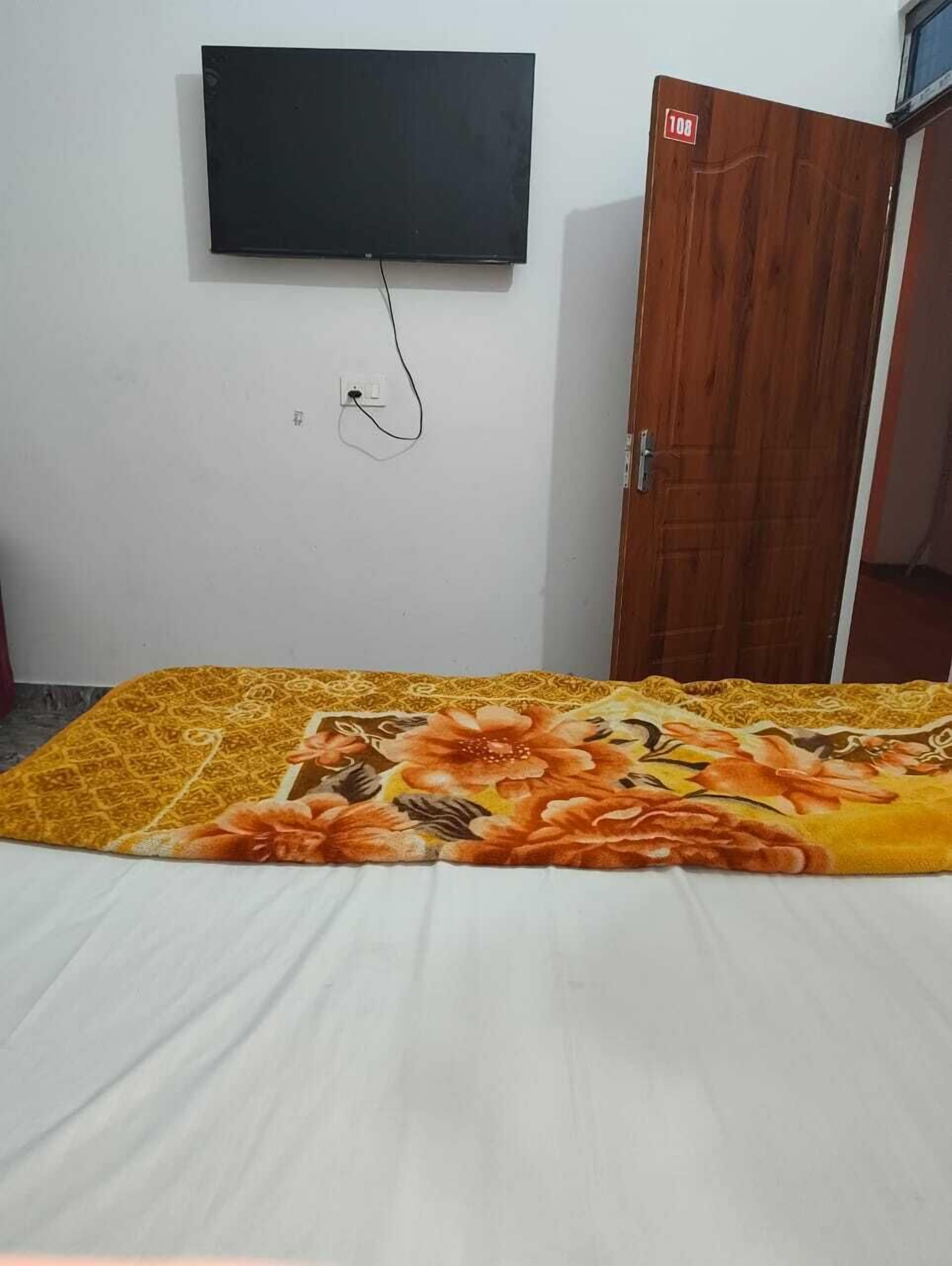 Un dormitorio con una cama, un televisor montado en la pared y una puerta de madera.