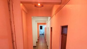 A long, narrow hallway with wooden flooring and white walls, leading to a door at the end. - Shubh Hotel (Phulpur)