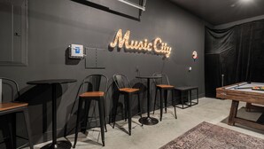 Une pièce avec une table de billard, quatre tabourets de bar et un panneau lumineux au néon sur le mur, sur lequel on peut lire « Music City ».