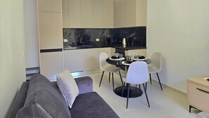 En moderne stue med en grå sofa, et spisebord med stole og et køkkenområde med skabe og en sort bordplade.