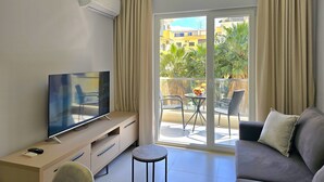 En moderne stue med et fladskærms-tv, en sofa, et rundt sofabord og en balkon med havemøbler.