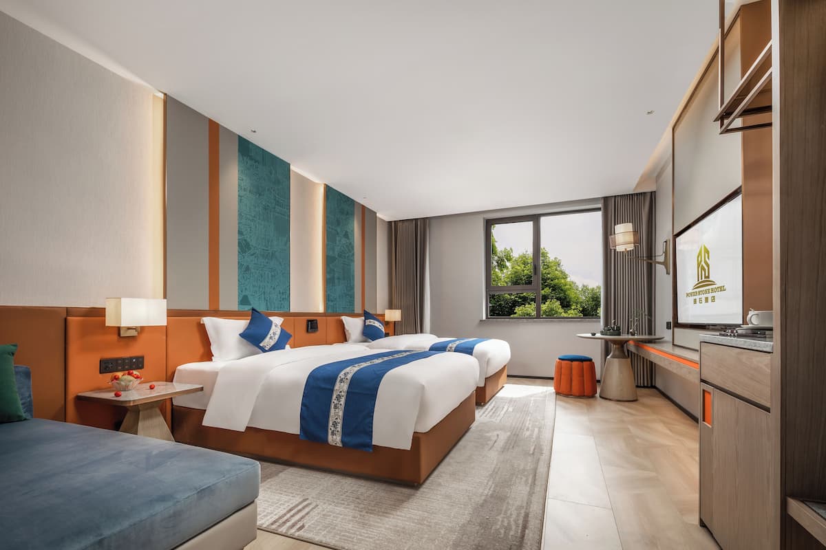 A modern hotel room with a large bed, a desk, and a view of greenery outside.