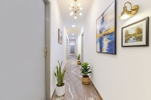 Un couloir doté d’un sol en marbre, de plantes en pot, d’œuvres d’art encadrées et d’une lampe fixée au mur.